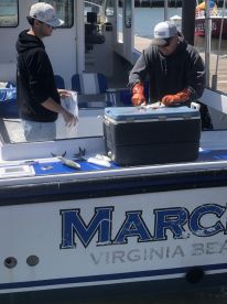 Two anglers preparing freshly caught fish on a boat in Virginia Beach, with a cooler visible for storage.