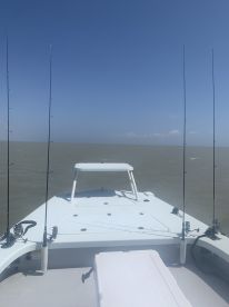View from the front of a fishing boat, showcasing the fishing rods and the calm waters of the Gulf Coast under a clear blue sky.