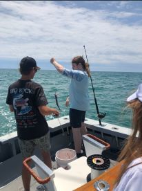 Two young anglers on a boat, with one proudly displaying a fish just caught while the other observes, showcasing an exciting moment during a fishing trip.