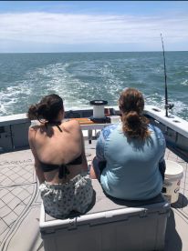 Two young anglers enjoying a day on the water, seated on a cooler in the boat, with fishing gear visible in the background.