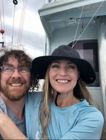 Two smiling individuals enjoying their time on a fishing boat, showcasing a friendly atmosphere onboard.