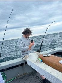 A fisherman sitting on the boat, focused on his phone while waiting for a catch in the open sea.