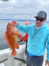 Angler proudly displaying a large rockfish while fishing on a boat in open waters.