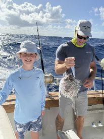 A young angler smiles proudly while holding a pufferfish on a fishing charter in open waters.