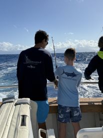 A young angler and an adult are engaged in fishing on a boat, with a beautiful ocean backdrop, showcasing the excitement of deep-sea fishing.
