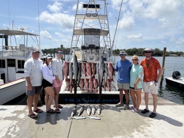 A group of anglers proudly posing with their catch of Red Snapper and other species displayed on a catch board at the dock after a successful fishing trip.