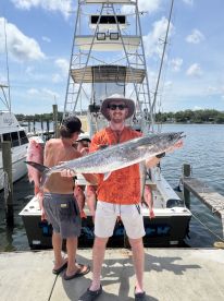 Angler proudly displaying a large King Mackerel alongside several Snapper at the dock after a successful fishing trip.