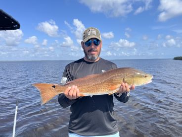 Angler proudly displaying a large Redfish while fishing in a scenic coastal environment.