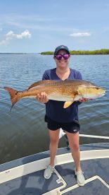 An angler proudly displaying a large Redfish while fishing in a scenic coastal environment.
