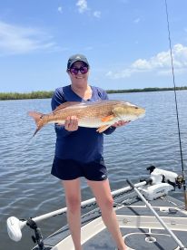 An angler proudly displaying a large Redfish while fishing on a sunny day in a coastal waterway.
