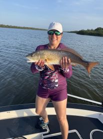 An angler proudly displaying a large Redfish while fishing on a boat in a scenic waterway.
