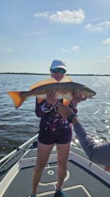 An angler proudly displaying a large Redfish while on a boat in a scenic fishing environment.