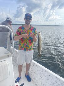 An angler proudly displaying a large Speckled Trout while fishing from a boat in a scenic waterway.