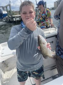 A young angler proudly displaying a freshly caught fish while fishing on a boat, surrounded by a scenic waterfront.