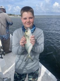 A young angler proudly displaying a small fish while fishing on a boat, enjoying a day on the water.