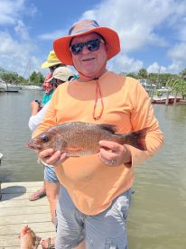 An angler proudly displaying a freshly caught Snapper while standing on the dock, with boats visible in the background.