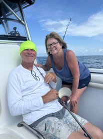 A couple enjoying their time on a fishing boat, with a scenic ocean backdrop and fishing gear visible.