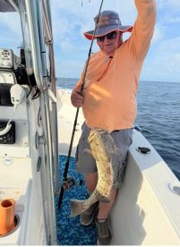 Angler holding a large Grouper while fishing on a boat, showcasing a successful catch in open waters.