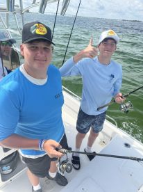 Two young anglers actively fishing on a boat, showcasing their enthusiasm while casting lines in a coastal waterway.