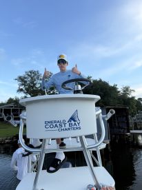 A young angler gives a thumbs up while seated at the helm of a charter boat, showcasing the boat's interior and branding for Emerald Coast Bay Charters.