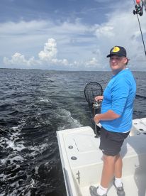 A young angler actively fishing from a boat, preparing to net a catch in a scenic waterway.