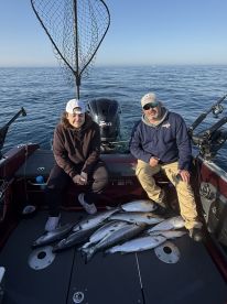 A young angler and an adult pose on a fishing boat with a successful catch of multiple salmon, showcasing their haul after a day on the water.