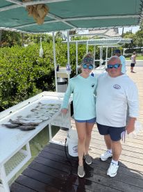 A group poses with their catch of various fish displayed on a cleaning table at a fishing dock, showcasing a successful day of fishing.