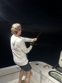 A young angler reeling in a catch during a nighttime fishing trip on a boat, showcasing the excitement of deep-sea fishing.