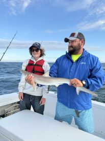 A young angler proudly displaying a caught shark while fishing on a boat, showcasing a fun day out on the water.