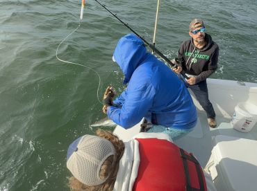 Anglers actively engaged in reeling in a fish while on a fishing charter, showcasing the excitement of the catch.