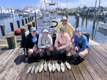 A group of anglers proudly displaying their catch of several fish on a dock after a successful inshore fishing trip.