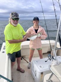 A young angler proudly displays a caught fish alongside an experienced fisherman on a boat, enjoying a day of fishing in open waters.