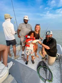 A young boy in a life jacket proudly holds a fish while surrounded by family members on a fishing boat, enjoying a day out on the water.