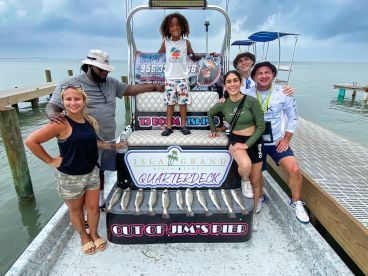 A diverse group of anglers proudly displaying their catch of Speckled Trout on a charter boat at Jim's Pier, showcasing a fun family fishing experience.