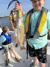 Young angler proudly displaying a Redfish while fishing on a boat, surrounded by family members enjoying a day on the water.