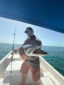 An angler proudly displaying a large Barracuda while fishing on a boat in clear blue waters.
