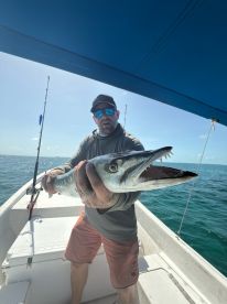 An angler proudly displaying a large Barracuda while fishing on a boat in clear blue waters.