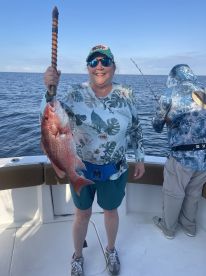 An adult angler proudly displaying a large Red Snapper while fishing offshore, showcasing a beautiful day on the water.