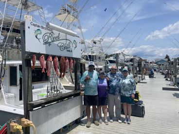 A group of four anglers proudly posing in front of a catch board displaying several Red Snapper at a marina in Destin, Florida.
