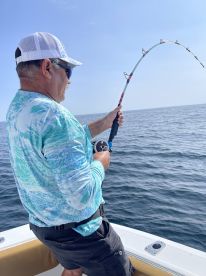 An angler actively reeling in a fish while fishing on a boat in open waters, showcasing the excitement of the catch.