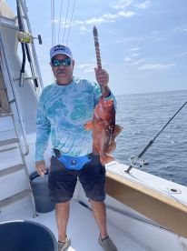 Angler proudly displaying a large Red Grouper aboard a fishing charter in open waters.