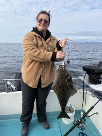 Angler proudly displaying a large Halibut while fishing on a boat in open waters.