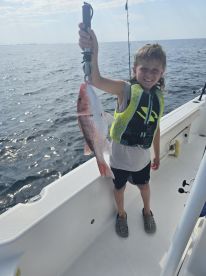 A young angler proudly displaying a freshly caught Red Snapper while fishing on a boat.