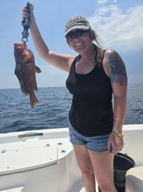 An angler proudly displaying a large Grouper while fishing on a sunny day at sea.