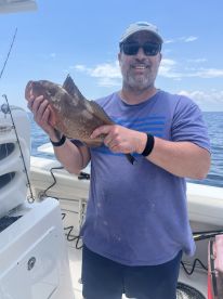 An angler proudly displaying a large Grouper caught while fishing offshore, showcasing a sunny day on the water.