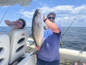 A proud angler displaying a large fish while a young companion poses playfully in the background on a fishing boat.