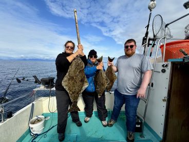 Three anglers proudly displaying their catch of Halibut aboard a fishing boat in open waters.