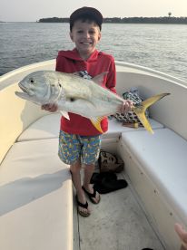 Young angler proudly holding a large Jack Crevalle aboard a boat, showcasing a successful fishing trip.