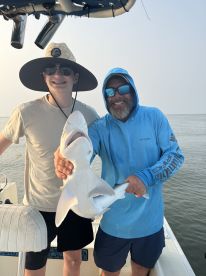 A young angler and an adult proudly displaying a caught shark while on a fishing boat, showcasing a successful day on the water.