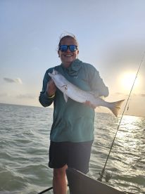 Angler proudly displaying a large Speckled Trout while fishing on a boat during sunset.